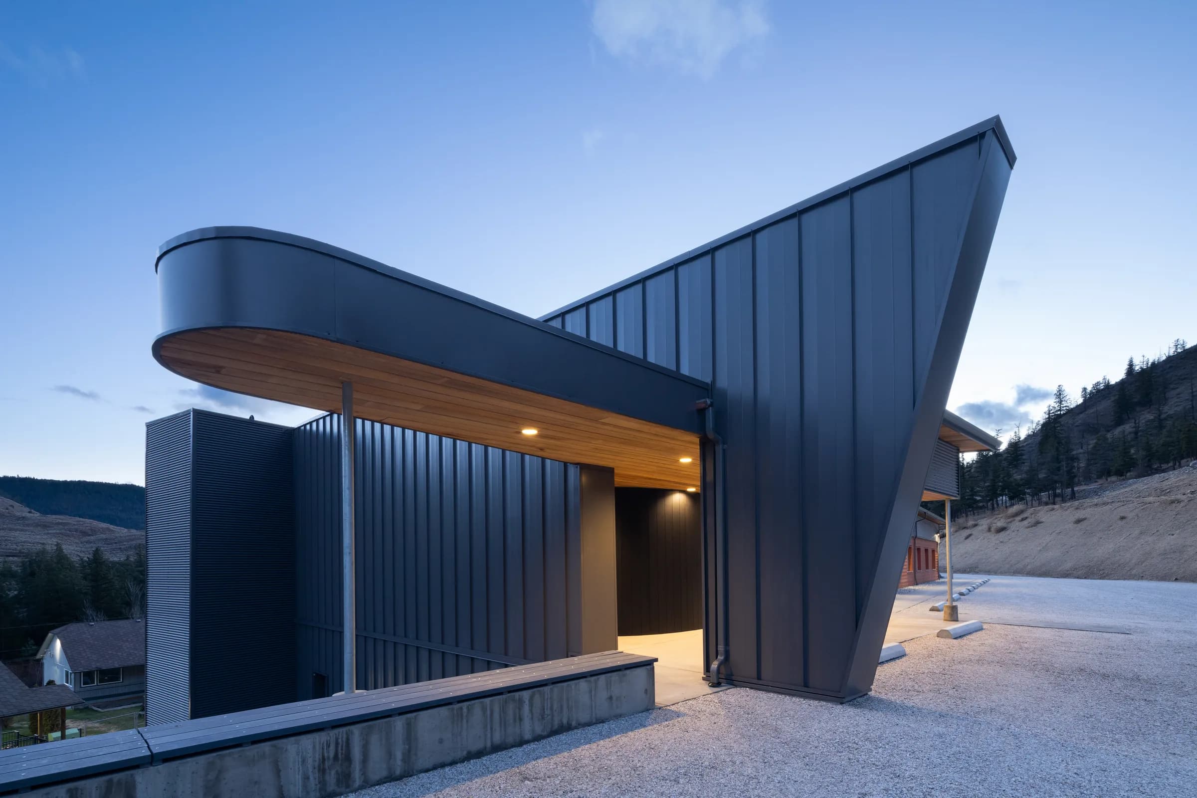 The upper entrance canopy and its curved timber soffit, with the surrounding hillside beyond mark a casual seathing area.